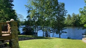 Ett grönområde utomhus med en stenpelare, ett trädäck och utsikt över en sjö som omges av träd.