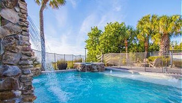 A swimming pool with clear blue water, surrounded by a stone wall and palm trees, indicating a tropical setting. - Beautiful Beachfront Home with Private Pool/ Firepit /on the Gulf (Indian Rocks Beach)