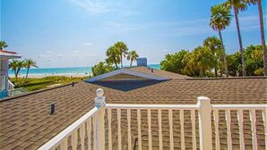 A beach view from a balcony with a white railing, palm trees, and a clear sky. - Beautiful Beachfront Home with Private Pool/ Firepit /on the Gulf (Indian Rocks Beach)