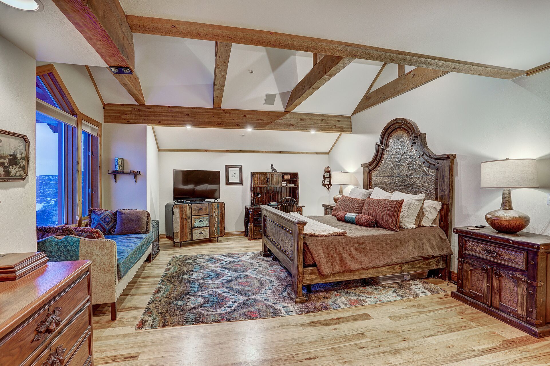 A bedroom with a wooden ceiling, a large bed, a television, and a view of the outdoors.
