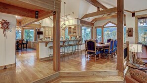 A spacious kitchen with wooden beams, a dining area with blue chairs, and large windows offering a view of the outdoors. - 🏆 Breck Private Estate | Hot Tub | 360° Views | 7 Acres (Breckenridge)