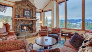 A cozy living room with a stone fireplace, large windows offering mountain views, and comfortable seating. - 🏆 Breck Private Estate | Hot Tub | 360° Views | 7 Acres (Breckenridge)