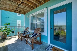 A covered porch with two wooden Adirondack chairs, a potted plant, and a blue door with a window. - Nature's Landing B204 Stargazer on the Gulf (Cedar Key)