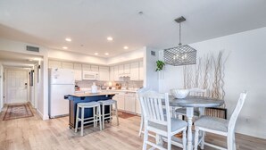 Una cocina moderna con armarios blancos, una isla central y un comedor con una mesa redonda y sillas blancas.