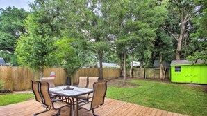 Um deck de madeira com uma mesa e cadeiras, cercado por um muro de madeira e árvores.