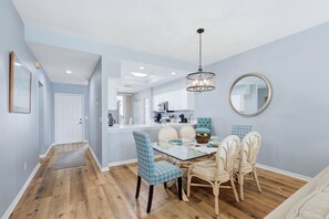 A dining area with a glass table, blue patterned chairs, a chandelier, and a round mirror on the wall.