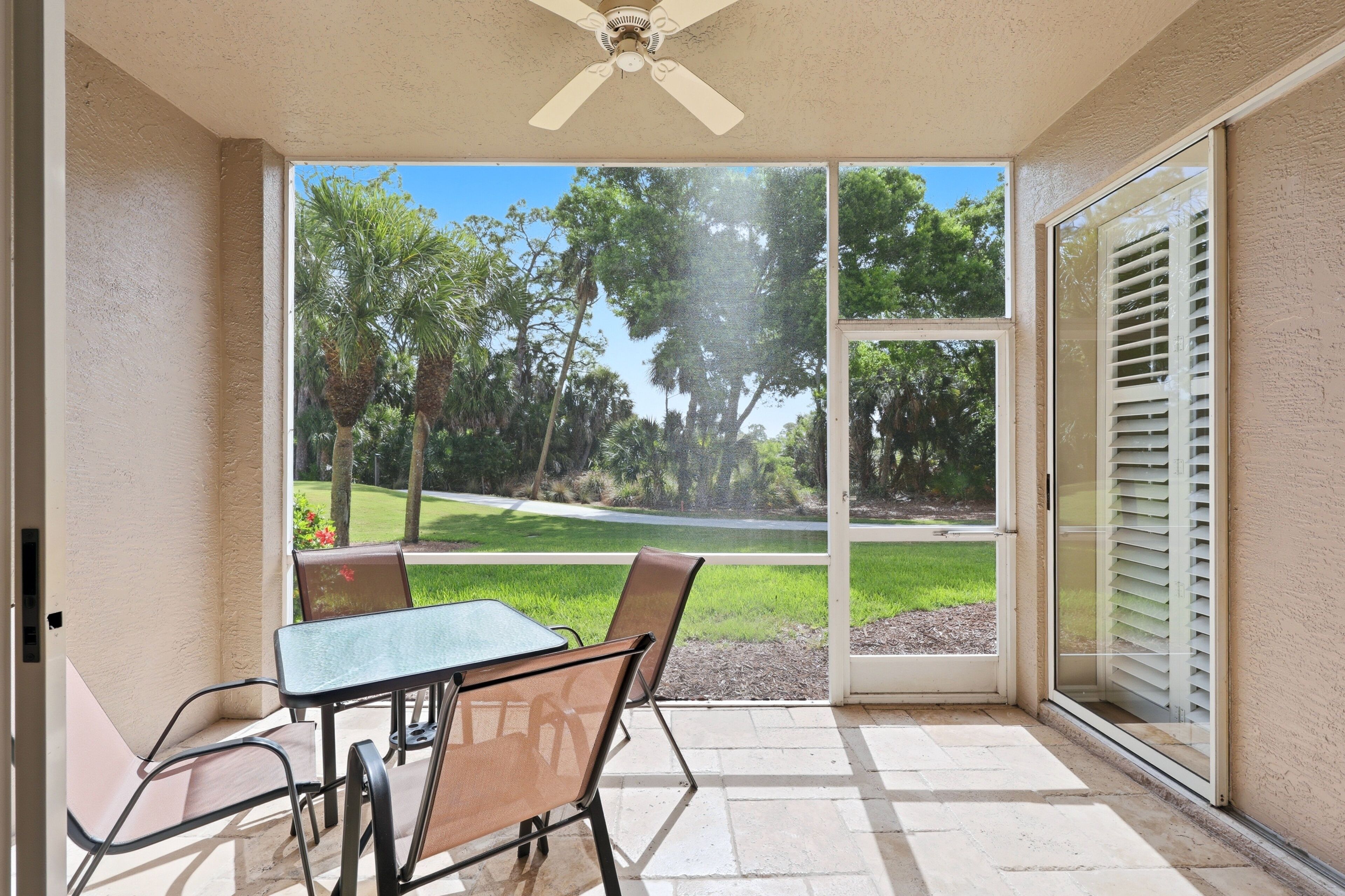 A covered patio with a table and chairs, a ceiling fan, and a view of a lawn and trees.
