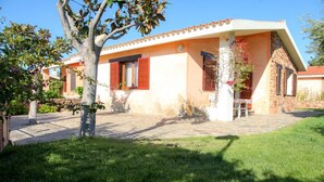 Una casa de dos pisos con techo de tejas, pared de piedra y un pequeño porche con una silla.