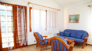 Una habitación con un sofá de madera, dos sillas de madera, una mesita y una puerta con cortinas.