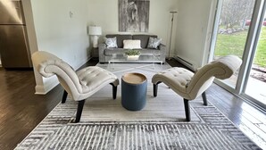 Een moderne woonkamer met een grijze bank, twee fauteuils, een salontafel en een groot raam.