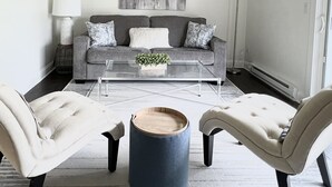 Een moderne woonkamer met een grijze bank, twee fauteuils, een salontafel en een vloerlamp.