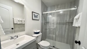 Een moderne badkamer met een wit wastafelmeubel, toilet en een douche met glazen wanden.
