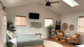 Ein Schlafzimmer mit einem Bett, einem Deckenventilator, einem Fernseher und einem Fenster.