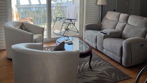 Una sala de estar con sofá, sillón y mesa de centro de vidrio.