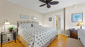 Un dormitorio con cama, mesitas de noche, ventilador de techo y puerta que da a otra habitación.