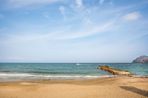 Une plage avec un ciel dégagé, une eau calme et un promontoire rocheux.