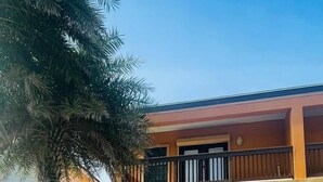Un edificio de dos pisos con garaje, un descapotable negro estacionado al frente y una palmera a la izquierda.