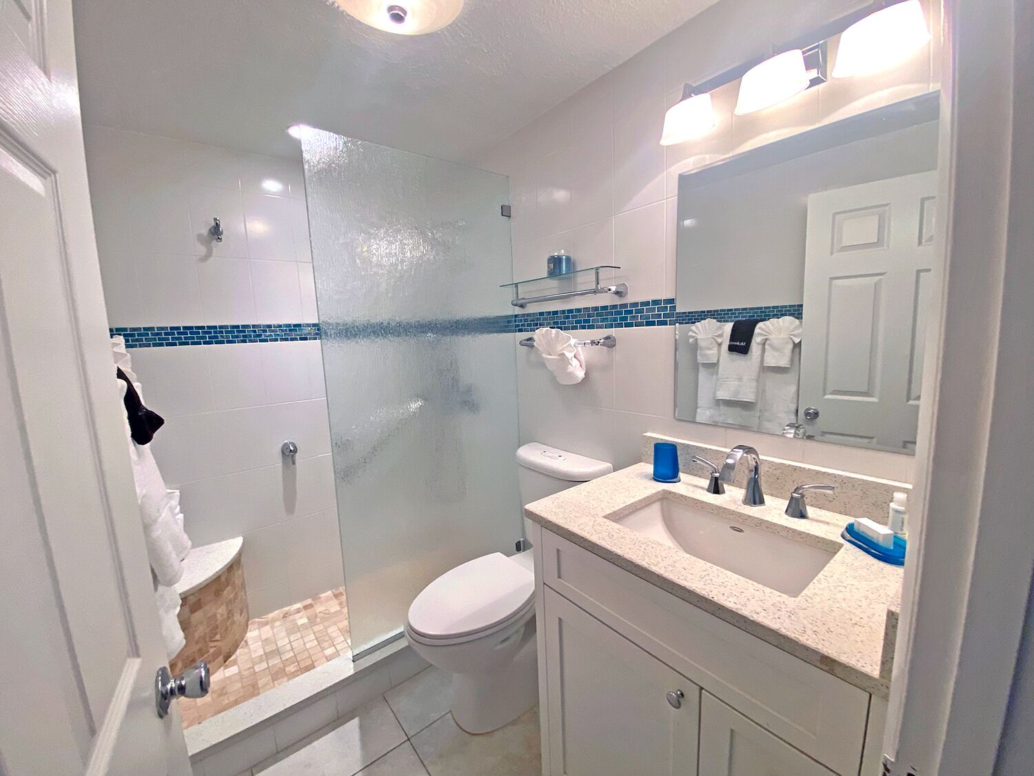 A bathroom with a glass shower enclosure, a toilet, a sink with a mirror, and a towel rack.