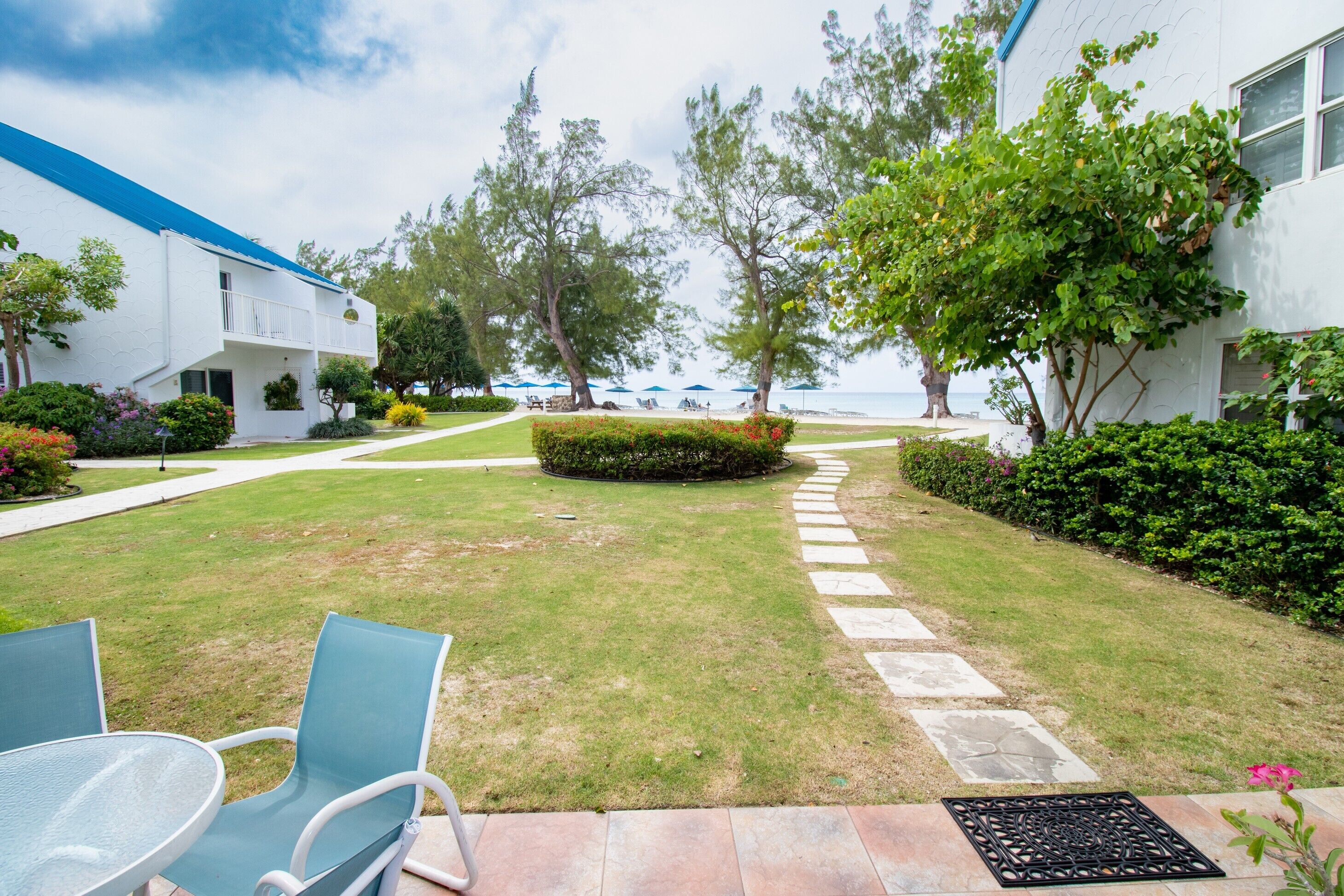 A courtyard with a lawn, a pathway, and a seating area with chairs and a table.