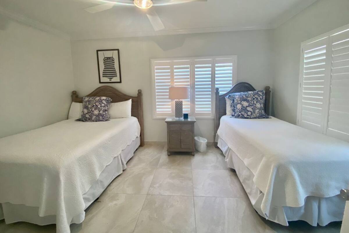 A bedroom with two single beds, a nightstand, a ceiling fan, and a window with blinds.