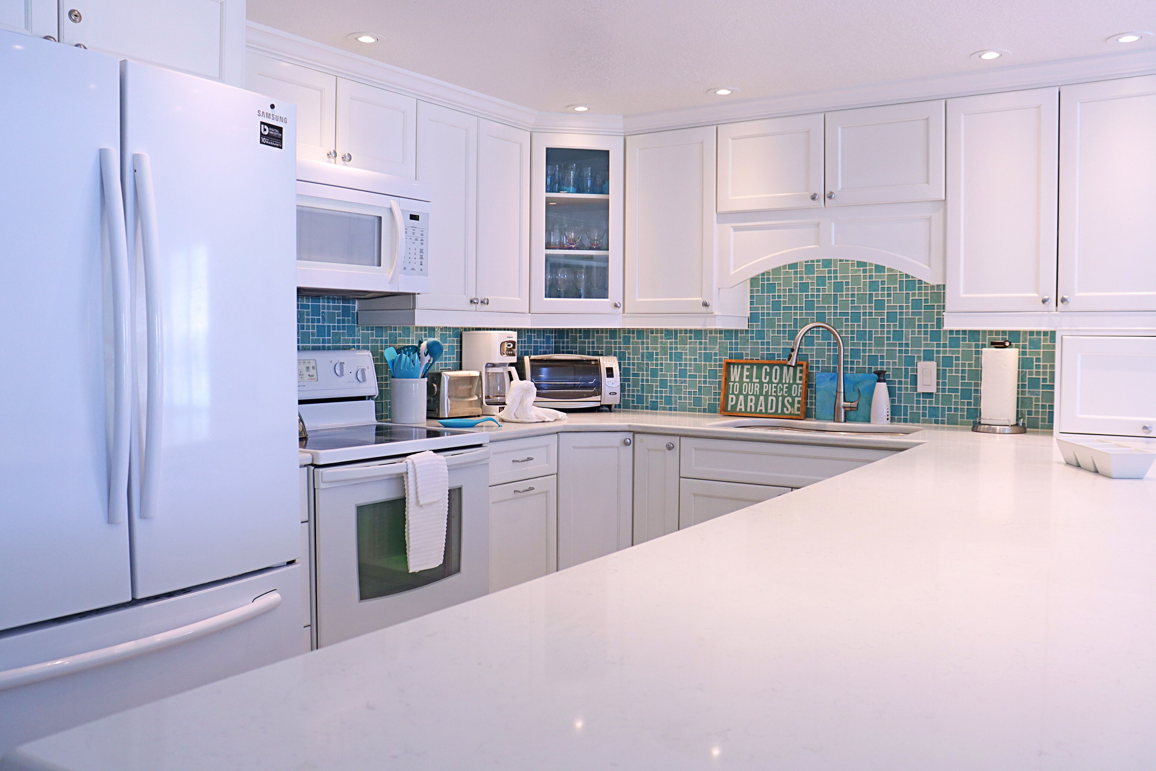 A modern kitchen with white cabinets, a white refrigerator, a microwave, a toaster, and a sink.