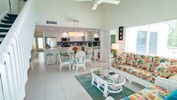 A spacious living area with a sofa, coffee table, and dining table. A staircase leads to an upper level.