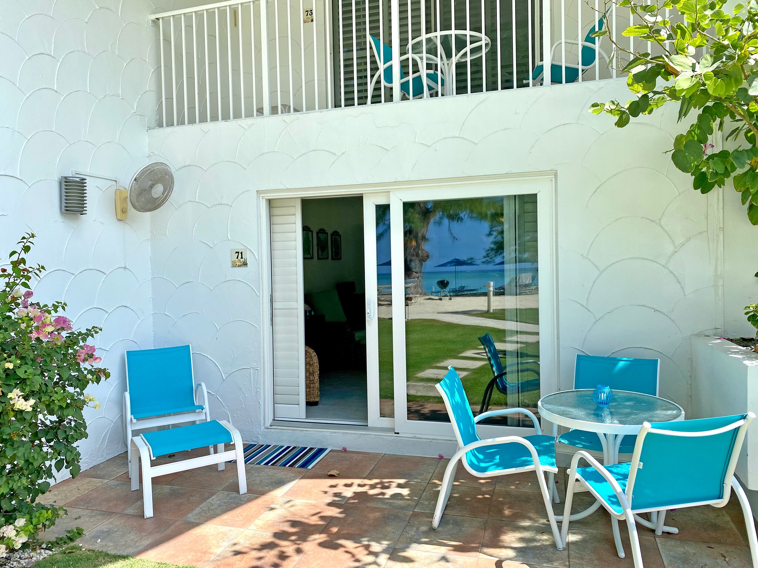 Un patio con una puerta de cristal que da a un balcón, mobiliario exterior y vistas a la playa.