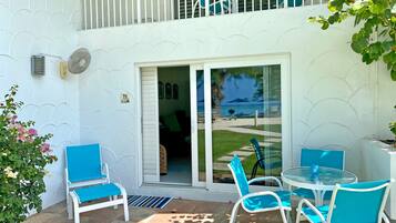 Un patio con una puerta de cristal que da a un balcón, mobiliario exterior y vistas a la playa.