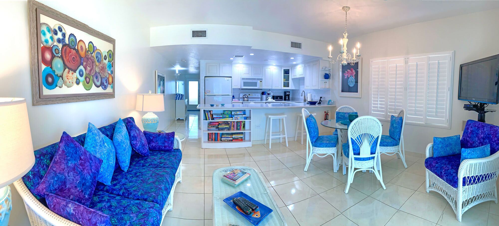 A modern living room with a blue sofa, white wicker chairs, a coffee table, and a bookshelf.