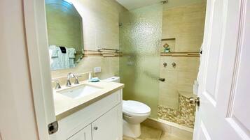 Ein Badezimmer mit zwei Waschbecken, einer Toilette und einer Duschkabine aus Glas.