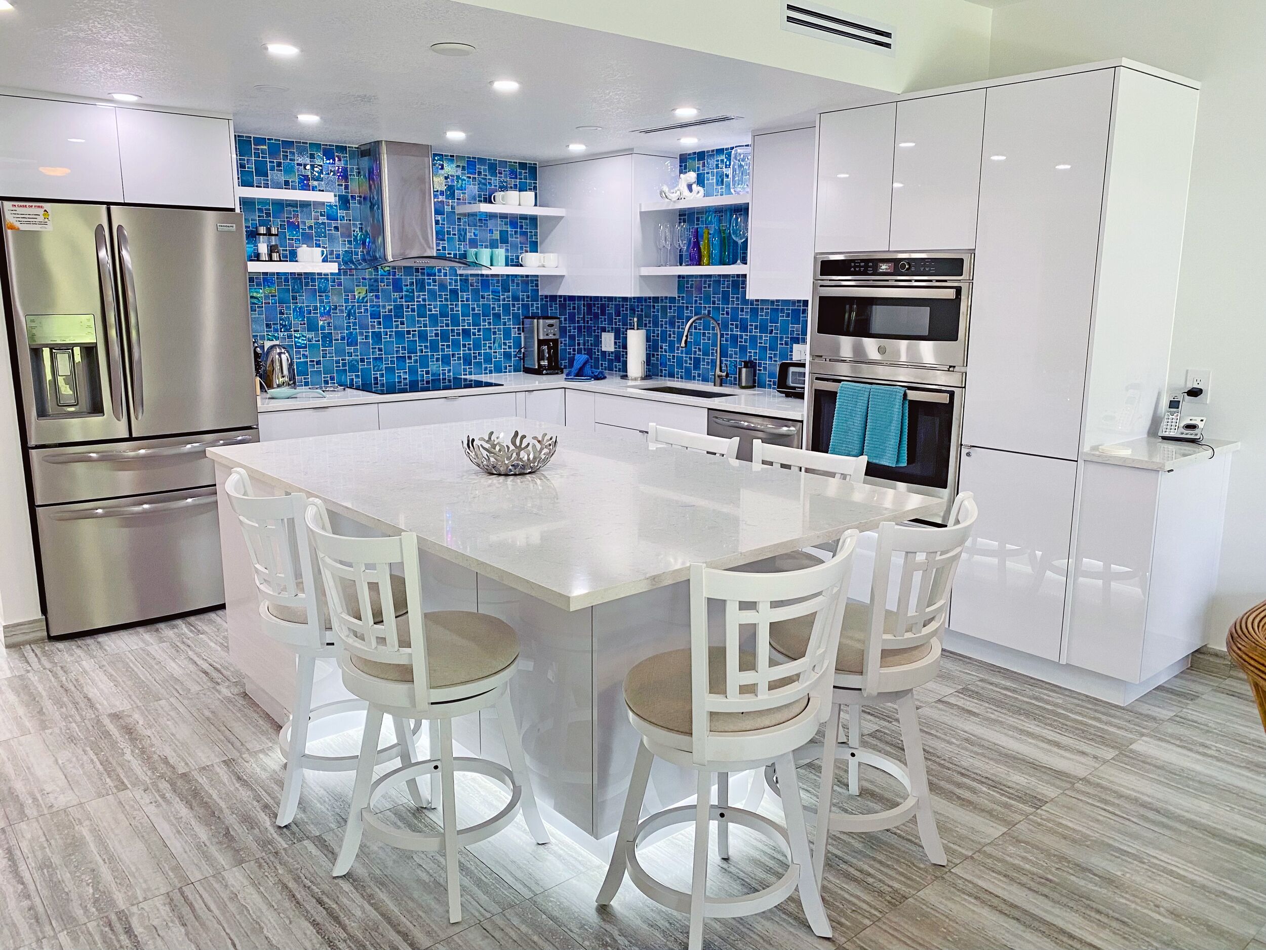 A modern kitchen with a central island, white cabinetry, and blue mosaic backsplash.
