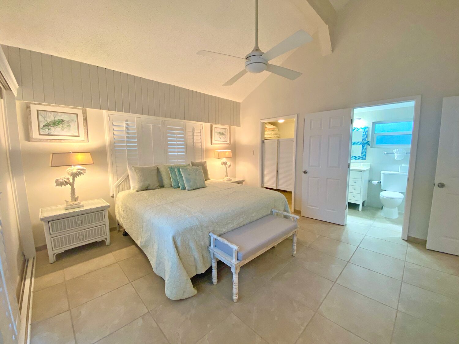 A bedroom with a bed, bedside tables, a ceiling fan, and a door leading to a bathroom.