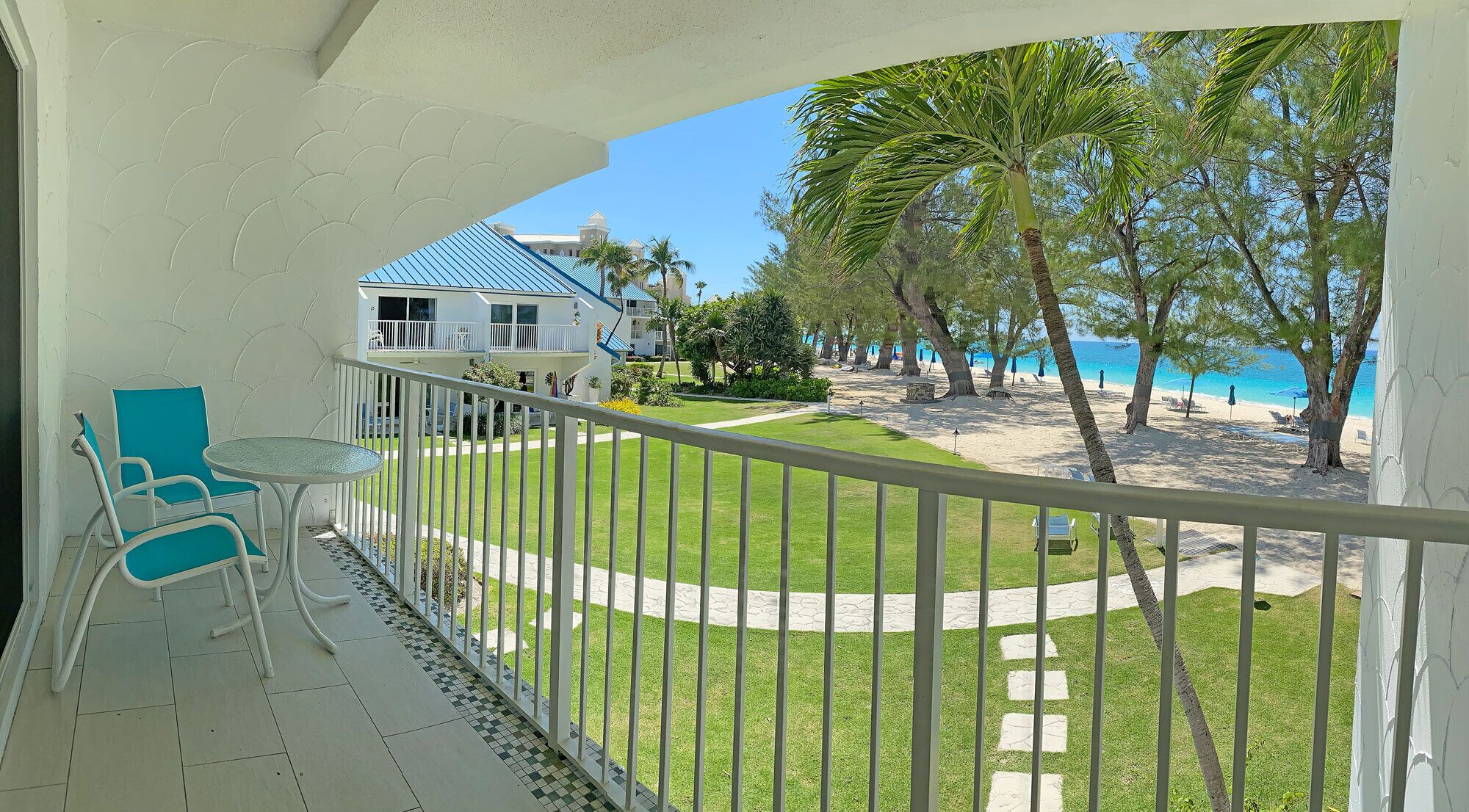 A balcony with a view of a beach, a house, and a lawn.