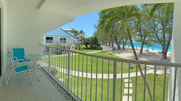 A balcony with a view of a beach, a house, and a lawn.