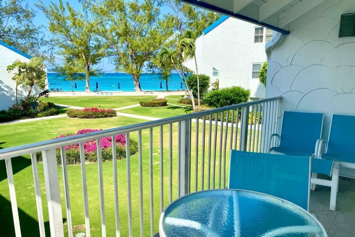 A balcony with a glass table, a view of the sea, and a well-maintained garden.