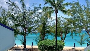 A balcony with a view of a beach, palm trees, and a clear sky.