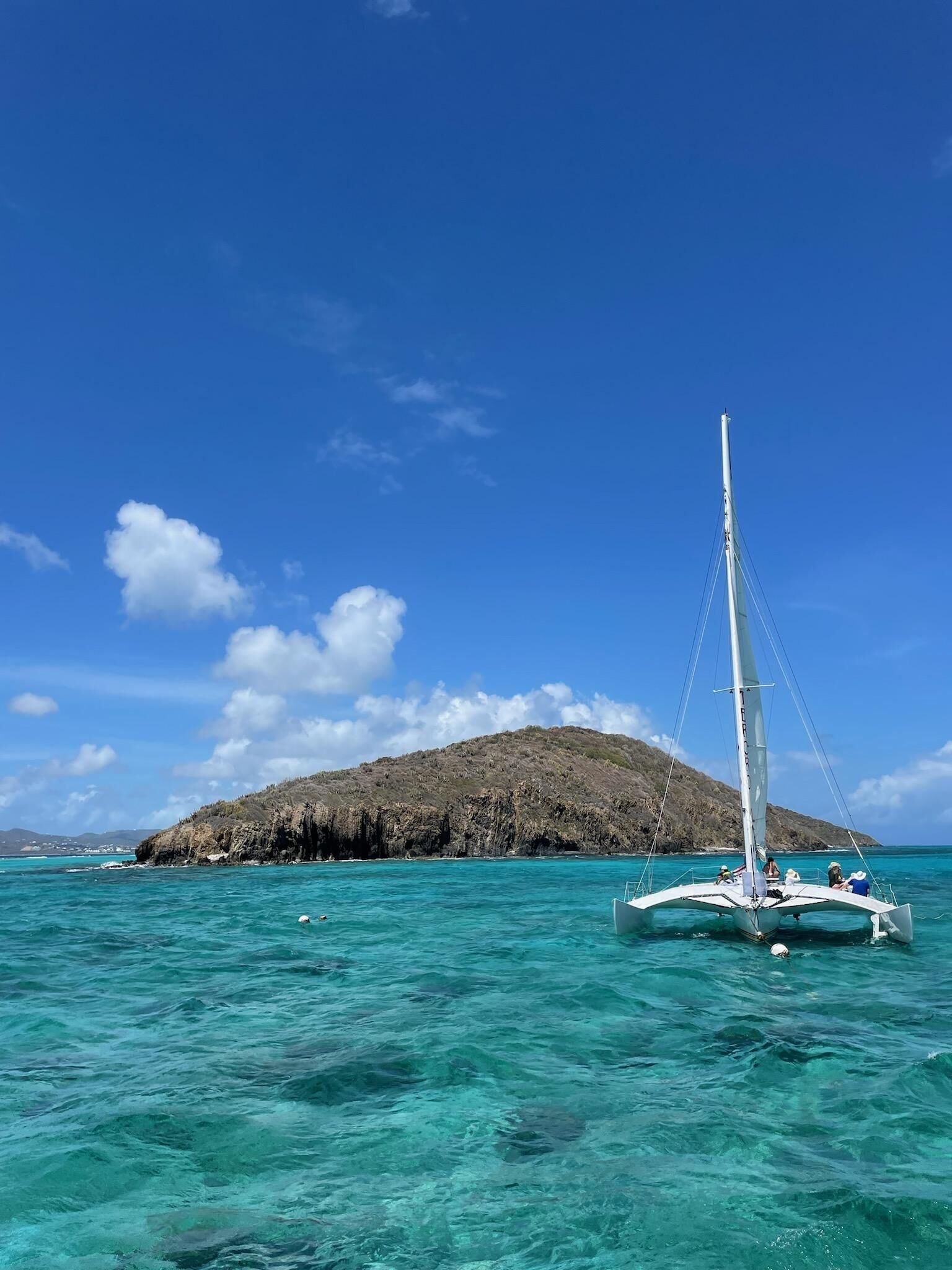A sailboat on turquoise waters with a rocky island in the background.