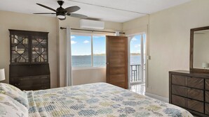 Un dormitorio con cama, ventilador de techo, armario y vista al mar a través de una puerta.