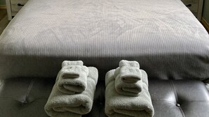 Cama bem arrumada com colcha cinza, dois travesseiros e cortina preta. Há duas mesas de cabeceira com luminárias e um quadro pequeno na parede.