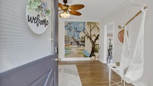 Un couloir agrémenté d’une pancarte de bienvenue, d’un ventilateur de plafond, d’un fauteuil suspendu et d’une fresque représentant l’église Sainte-Marie.