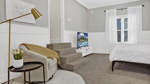 Une chambre à coucher avec un lit, un téléviseur posé sur un meuble, un canapé, une petite table avec une plante et un escalier.