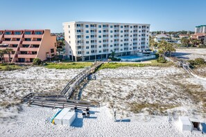 A beachfront hotel with a pool, multiple balconies, and a sandy beach area.