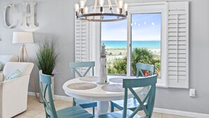 A dining area with a view of the beach, a chandelier, and a 'CH' sign on the wall.