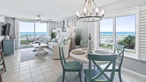 A spacious living area with a large window overlooking the beach, a chandelier, and a cozy seating arrangement.