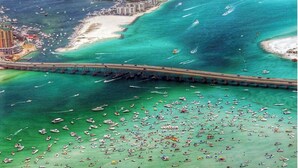 An aerial view of a coastal city with a prominent bridge, numerous boats, and a densely built urban area.