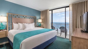 Habitación de hotel con una cama grande, un balcón con vistas al océano y un escritorio con televisor.