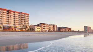 Un hotel frente a la playa con varias edificaciones, incluyendo un edificio grande con balcones y otro más pequeño con vista al mar.
