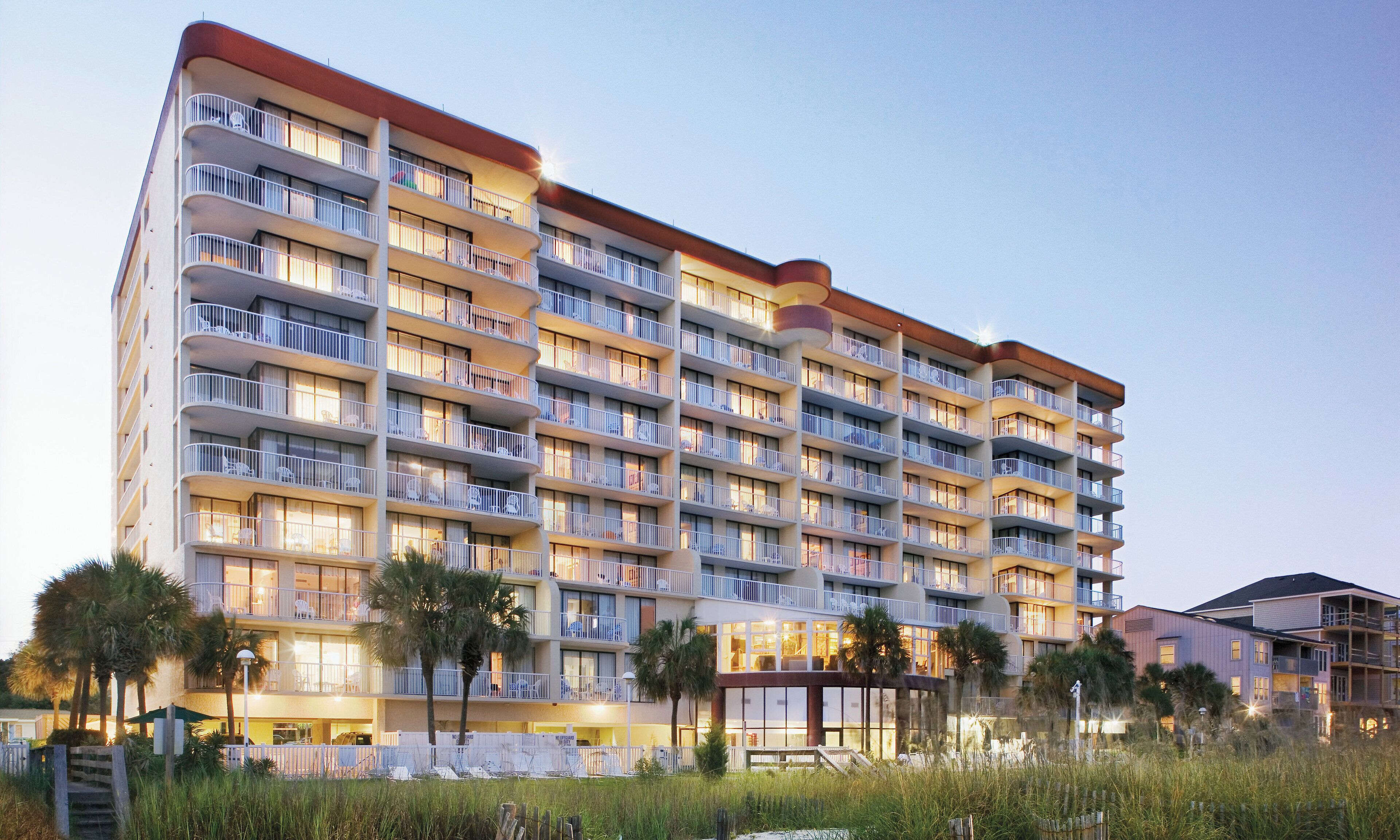 A multi-story hotel with balconies, a pool area, and a beach view.