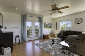 A spacious living room with a ceiling fan, a sofa, a coffee table, and a large window with curtains.