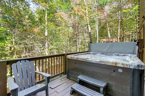 Una terraza de madera con un jacuzzi, una silla Adirondack de madera y un banco de madera.